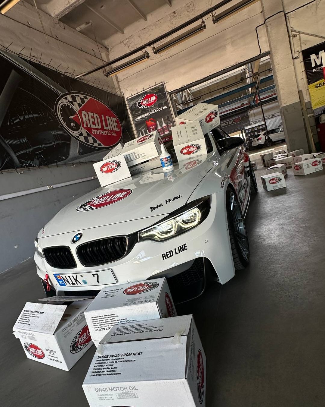 BMW M3 F80 albă de 1012 CP în colantul Red Line, în atelierul 4Power Club, înconjurată de cutii cu ulei Red Line